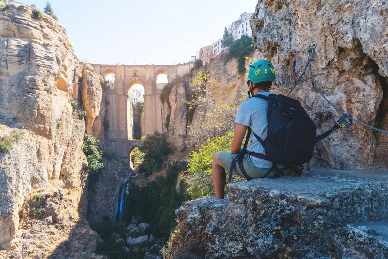 Una persona con casco y mochila mira el Puente Nuevo desde la roca del Tajo